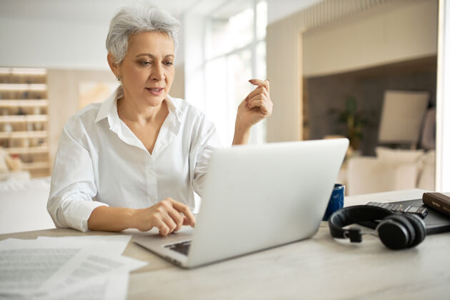 桌子时尚成熟的女商人 留着短发 坐在笔记本电脑前 张着嘴看着屏幕 好像在说什么通信笔记本电脑互联网