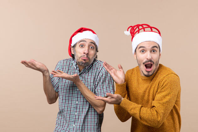 帽子正面图两个戴着圣诞老人帽子的家伙展示了一些米黄色的孤立背景两个惊奇的家伙两个男人