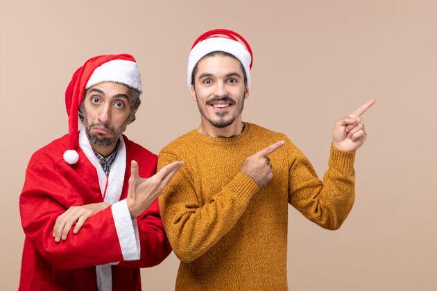 风景前视图两个戴着圣诞帽的朋友 一个在米色背景上展示东西米色前面朋友