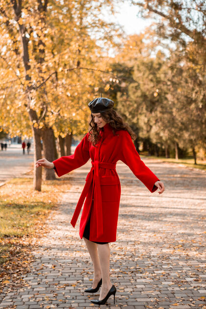 穿着迷人时尚的微笑瘦削女子卷发漫步公园穿着温暖的红色外套秋季时尚 街头风格 戴贝雷帽年轻户外优雅