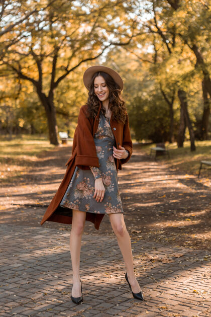 秋天迷人时尚微笑的女士 卷发漫步公园 身着印花连衣裙和保暖外套 秋季时尚 街头风格年轻优雅女人