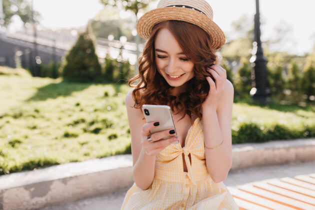 女性兴奋的戴着帽子的姜汁女孩微笑着发短信公园里性感红发女士与智能手机合影的户外写真人小工具年轻