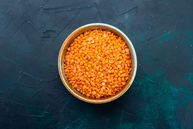 膳食深蓝色表面上圆形锅内的生橙色小扁豆俯视图桌子锅圆形