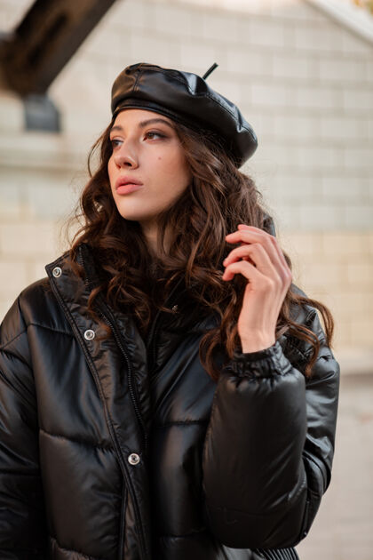 户外时尚女人摆出冬秋时尚潮流黑色羽绒服和皮帽贝雷帽在古老美丽的街道穿着高跟鞋服装街头风格优雅