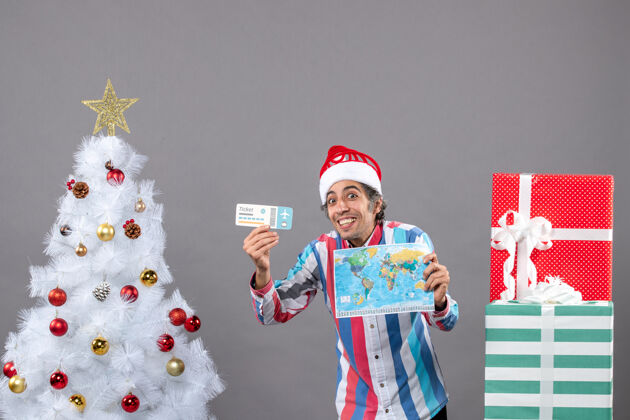 男正面是戴着螺旋弹簧圣诞帽的快乐男人 手里拿着世界地图和旅行票男圣诞节目的地
