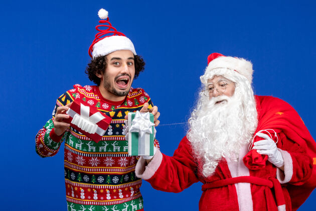 男人正面图：圣诞老人和手持礼物的年轻男性举行情感东方人