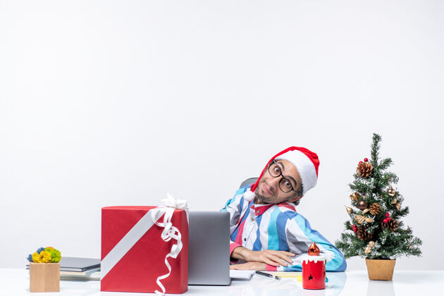 前面正面图：年轻的男工人坐在他工作的地方 背景是白色的办公室情感圣诞节