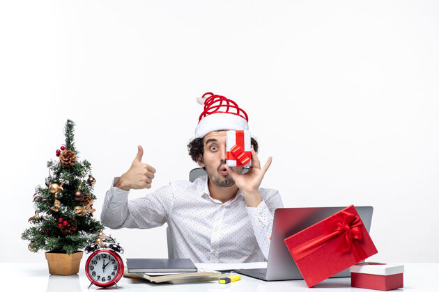 圣诞老人圣诞节心情与有趣的商人与圣诞老人的帽子提高他的礼物 他的脸 并作出完美的姿态在白色背景圣诞节手势圣诞老人