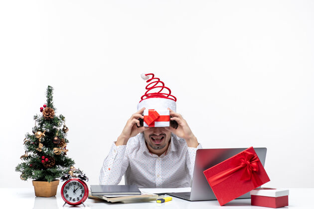 舌头圣诞节心情与有趣的商人圣诞老人帽子举行他的礼物在他面前 并伸出舌头在白色的背景圣诞老人礼物圣诞老人