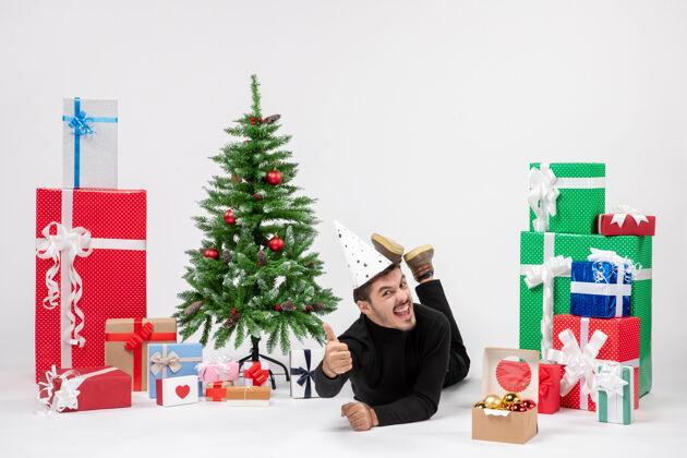 人年轻人躺在白色墙上的节日礼物周围的正面视图圣诞快乐插花快乐
