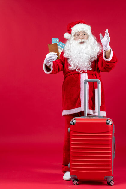 人圣诞老人的前视图 带着包 拿着票 准备在红墙上旅行旅行面子圣诞老人