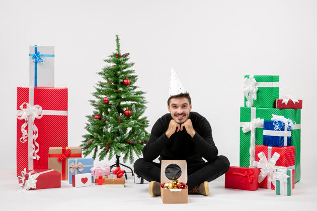 盒子年轻人坐在白色墙上的节日礼物周围的正面视图礼物礼物十二月