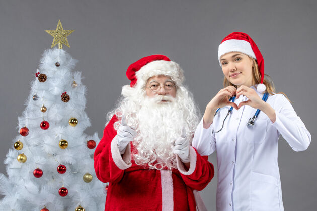 十二月圣诞老人和女医生在灰色墙上传递爱的正面图服装男人女性