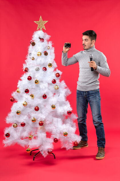 庆祝圣诞气氛严肃的年轻人站在装饰好的圣诞树旁拿着麦克风拍照麦克风装饰快乐