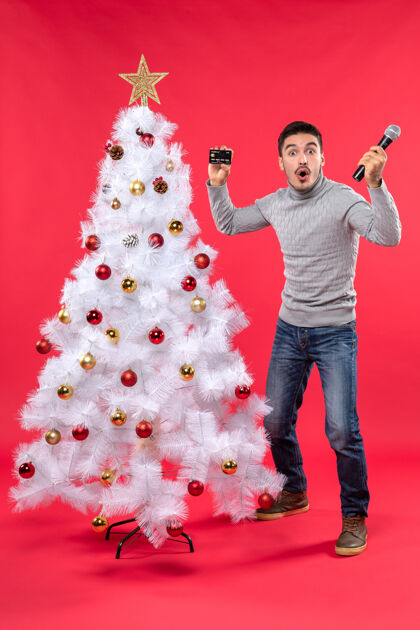 装饰圣诞节心情与惊喜有趣的家伙站在装饰圣诞树附近 手持麦克风拍照站立有趣采取