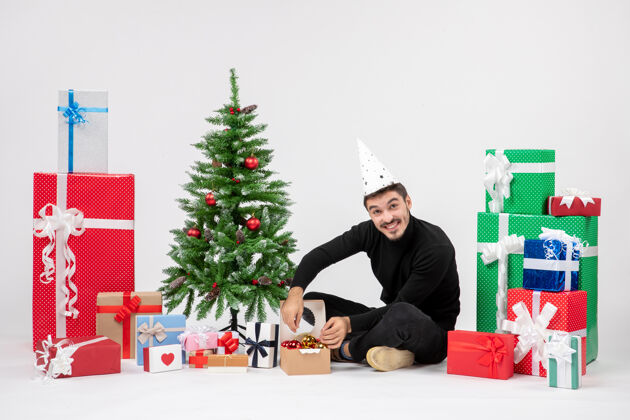 礼物年轻人围坐在节日礼物装饰白色墙上的小树的前视图圣诞快乐人人