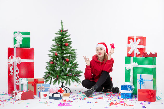 圣诞树正面图：年轻女子围坐在白色墙上 手里拿着红色的银行卡十二月银行情感