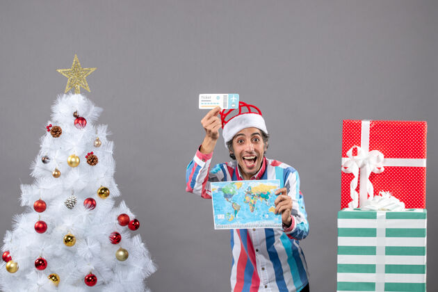 礼物正面图快乐的年轻人戴着螺旋弹簧圣诞帽拿着世界地图和旅行票人举行圣诞帽