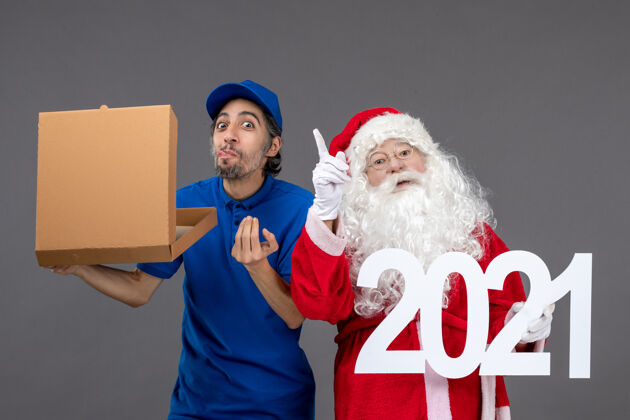 节日圣诞老人的正面图 男信使拿着购物袋和食品盒在灰色的墙上圣诞快乐食物