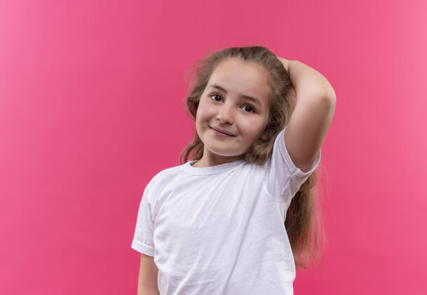 穿着微笑的小女孩穿着白色t恤 把她的手放在孤立的粉红色背景的头上白色女孩手