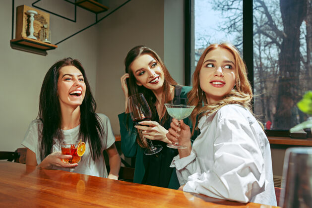 杯子女朋友在酒吧喝酒她们坐在一张摆着鸡尾酒的木桌旁她们穿着休闲服食物白天水果