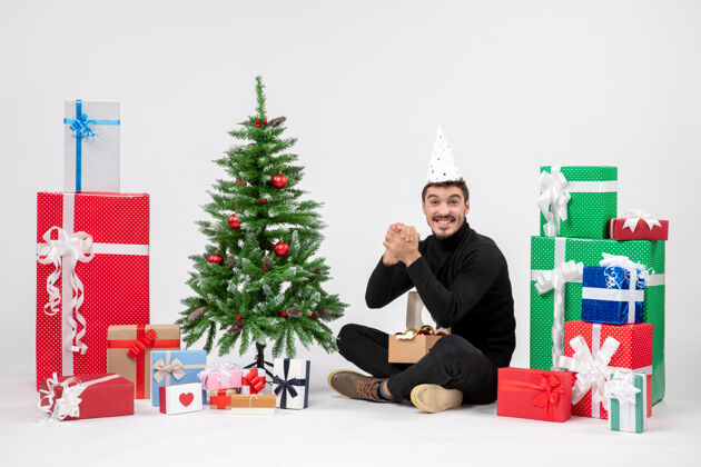 礼物年轻人坐在白色墙上的节日礼物周围的正面视图季节人十二月