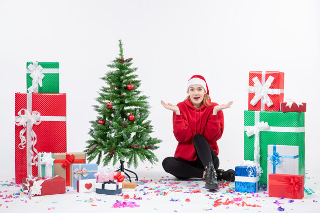 快乐年轻女子坐在白色墙壁上的节日礼物周围的正面视图庆祝情感季节
