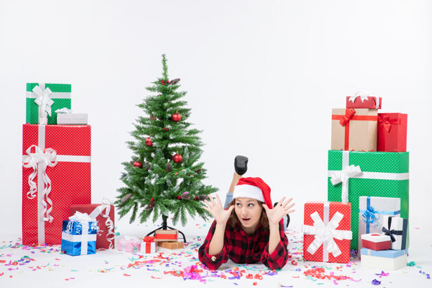 节日年轻女子躺在白色墙壁上的圣诞礼物和小圣诞树周围的正视图快乐小圣诞