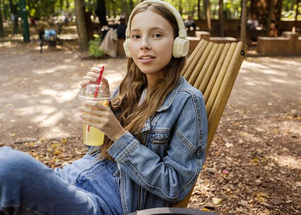 果汁戴着耳机拿着新鲜果汁的中镜头年轻女子热带水果热带饮料