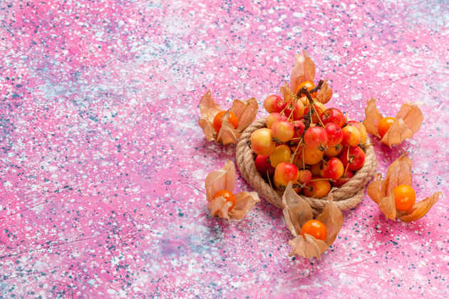 花在浅粉色的桌子上用绳子顶着新鲜的甜樱桃维管水果樱桃