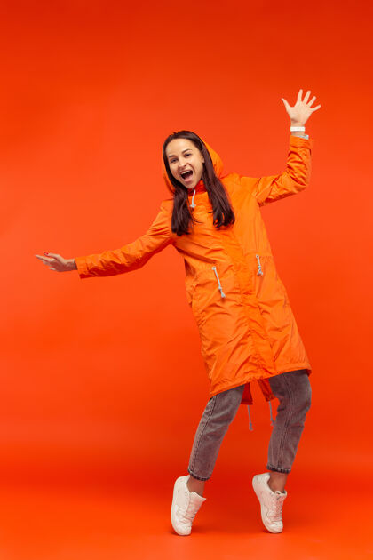 外套这个快乐微笑的年轻女孩穿着秋天的橘色夹克在摄影棚里摆姿势红色隔离人类积极的情感寒冷天气的概念女性时尚概念女性下雨微笑