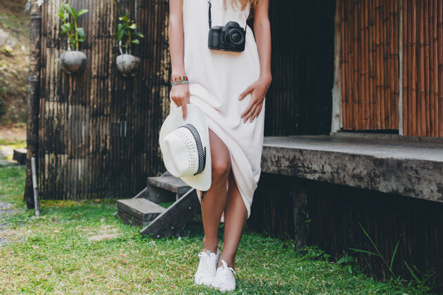 波西米亚亚洲热带度假的年轻美女 夏季风格 白色波西米亚裙 运动鞋 数码相机 旅行者 草帽 腿部特写细节女士鞋时尚