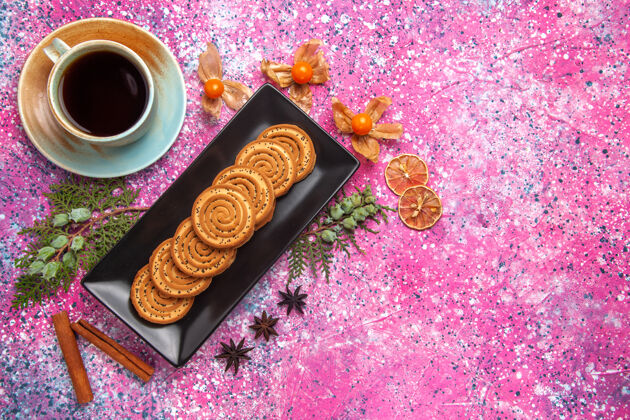 蛋糕顶视图中的甜饼干与肉桂和茶在浅粉红色的表面黑色形式饼干饼干里面