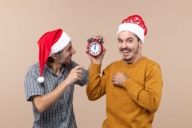 两个正面图两个快乐的男人 一个拿着闹钟 另一个在米色的背景上关掉闹钟米色两个快乐的男人脸