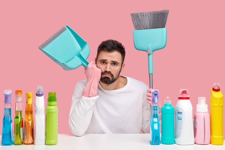 家务心烦疲惫的丈夫戴着粉色橡胶手套 拿着扫帚和勺子 扫地后休息 用清洁剂打扫房间摆姿势阴郁男性