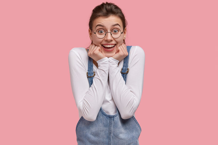 年轻人乐观的白种女人抱着下巴 积极地微笑 对生活中美好难忘的时刻感到高兴 咯咯地笑牙牙学语青少年眼镜