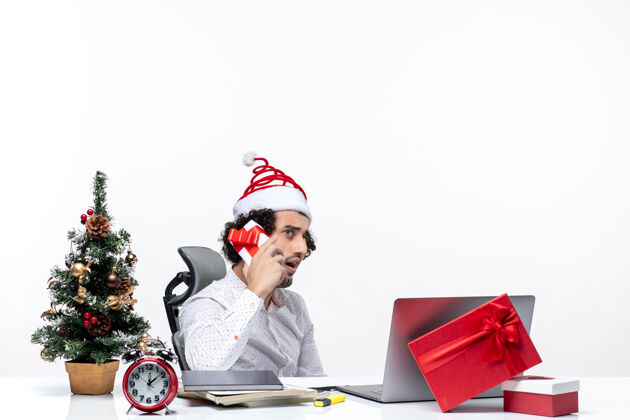 人圣诞节心情与年轻的胡须惊讶的商人圣诞老人帽子提高他的礼物 并在白色背景上看东西礼物东西商务