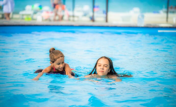 快乐两个小姐妹在海滩上的一个大游泳池里游泳小玩耍潮湿