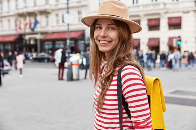 时髦照片中微笑开朗的女游客在城市里漫步感觉很好 戴着时髦的头饰和条纹套头衫街道高兴帽子