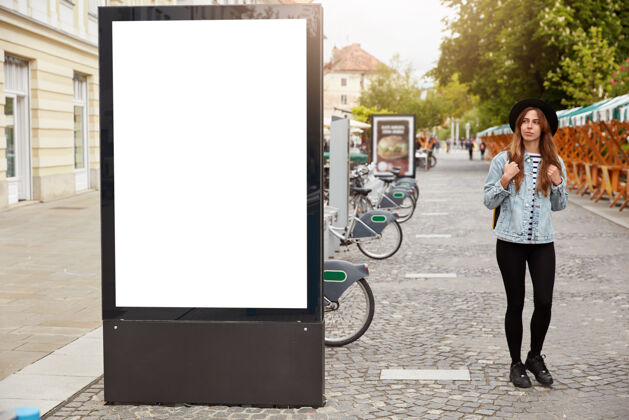 框架体贴的女性游客漫步在灯箱附近的人行道上 模型空白处为您提供广告内容或商业信息街头风格概念关注人行道上的广告牌空白女性灯箱