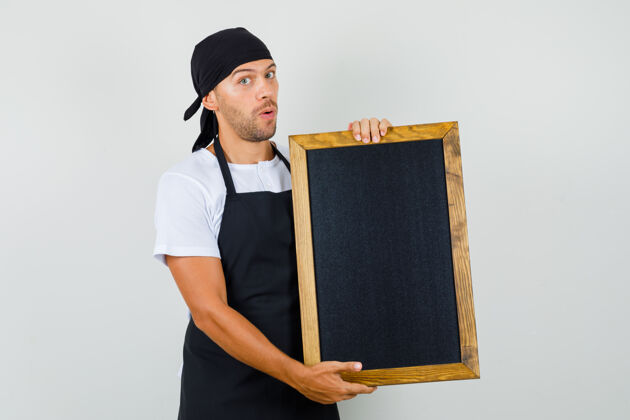 男性面包师穿着t恤 围裙拿着黑板 看上去很困惑美食家工作厨师