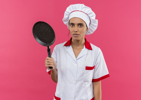 厨师惊讶的年轻女厨师穿着厨师制服拿着煎锅与副本空间穿着女制服