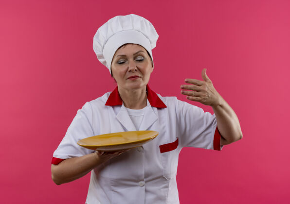 中年闭着眼睛的中年女厨师穿着厨师制服 拿着盘子嗅封闭制服女