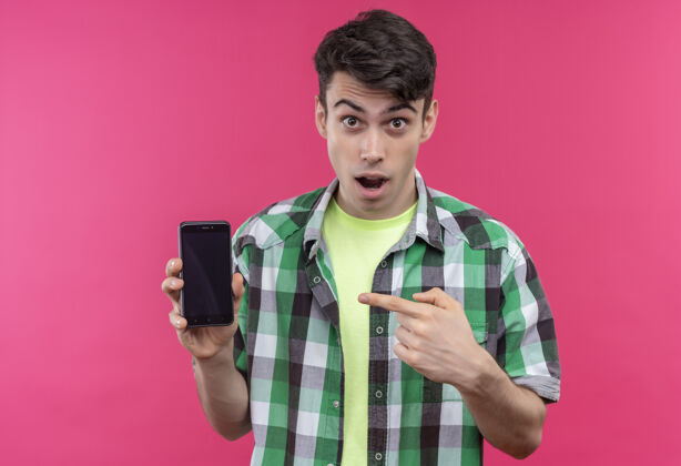 年轻一个穿着绿色衬衫的白人年轻人拿着手机指着孤立的粉色背景点衬衫粉色