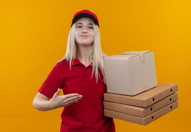 T恤一个穿着红色t恤和帽子的年轻女孩在孤立的橙色背景上指着手上的盒子手盒子点