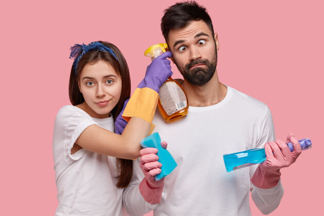 男朋友有趣的没刮胡子的男人交叉眼睛 帮妻子打扫房子 一起工作 做家务 用洗涤剂 海绵杂务搞笑墙