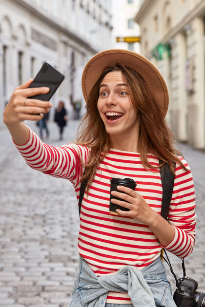 乐观喜出望外的欧洲女游客戴着帽子 在户外自拍 在古镇游览时玩得很开心手机女士电话