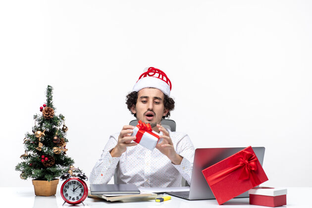 圣诞老人圣诞节心情严肃忙碌的商务人士与圣诞老人的帽子举起他的礼物 看着它在白色的背景看小孩严肃