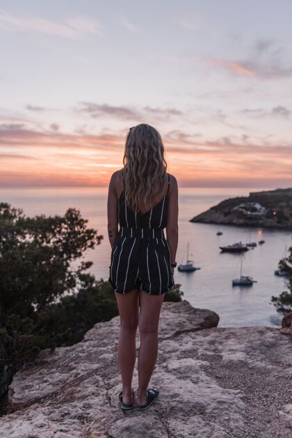 女人白天站在美丽的海边悬崖上的迷人的年轻女子度假黎明人