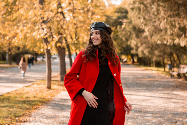 装束迷人的时尚微笑的女人卷发漫步在公园穿着温暖的红色外套秋季时尚 街头风格 戴贝雷帽穿着配饰优雅